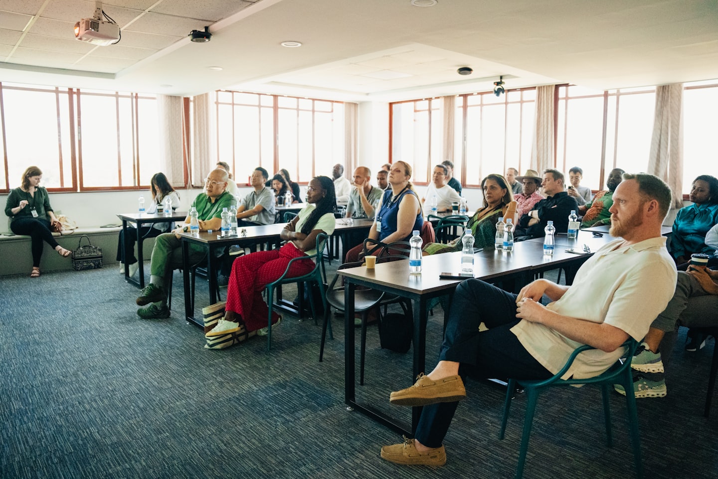 Dorośli uczestniczą w profesjonalnej konferencji, robiąc notatki przy stołach.