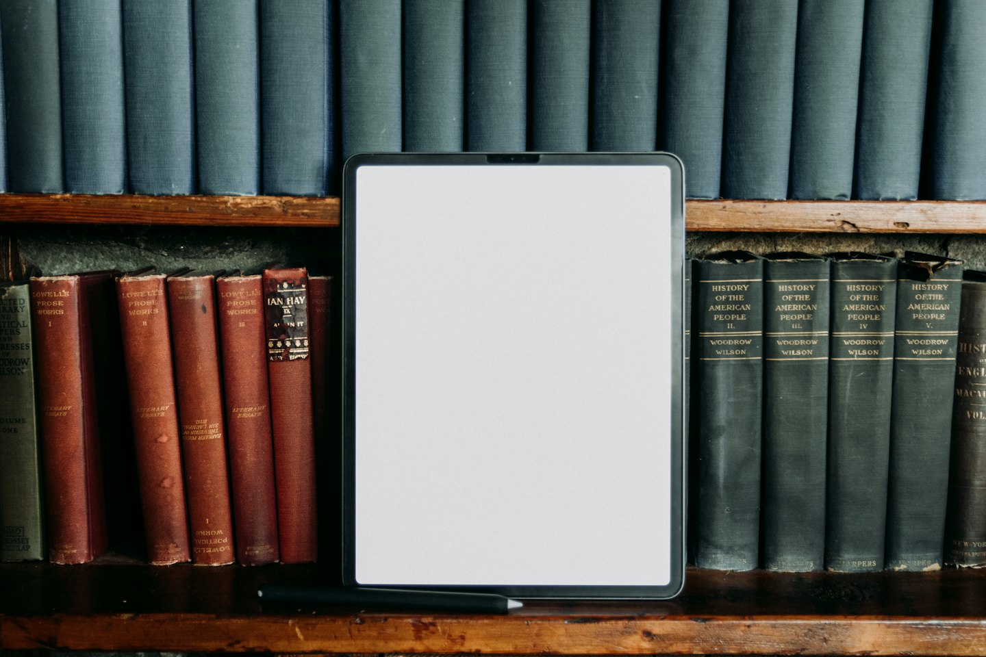 Tablet i stare książki na drewnianej półce.